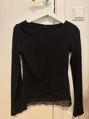Svart ribbad topp med spets från Gina Tricot - Svart långärmad topp från Gina Tricot i ribbat material. Toppen har en snygg spetskant nertill som ger en extra detalj. Perfekt att styla med jeans eller kjol för en trendig look.