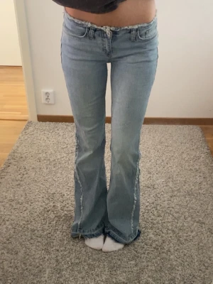 Ljusblå bootcut jeans med fransade kanter - Snygga lågmidjade bootcut jeans med fransade detaljer längs sidorna och på bakfickorna. Jeansen passar även om man har storlek 32