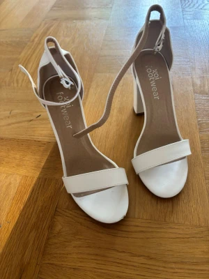 Vita blockklackade pumps från koi footwear - Snygga vita pumps från koi Footwear med öppen tå, bred rem över foten och justerbar ankelrem. Skorna är lite slitna framtill.