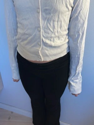 Vit croppad kofta med knappar - Snygg vit croppad kofta med långa ärmar och knäppning framtill. Koftan har en enkel och stilren design, perfekt att matcha med både jeans och kjol. Materialet är mjukt och stretchigt för en bekväm passform.