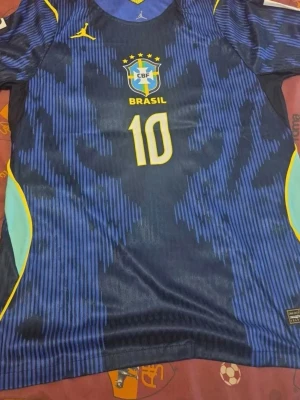 Blå Brasilien fotbollströja Neymar Jr - Snygg blå Brasilien fotbollströja från Nike med Neymar Jr och nummer 10 på ryggen. Tröjan har gula och ljusblå detaljer, CBF-emblem på bröstet och är tillverkad i ett lätt, ventilerande material perfekt för träning eller match.