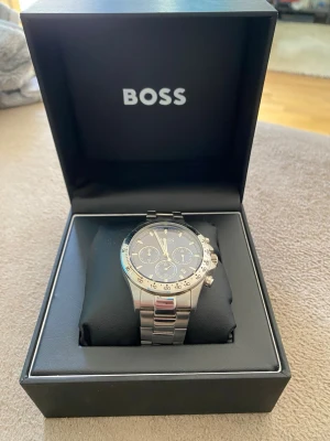 Hugo Boss  - Stilren klocka från Hugo Boss med silverfärgat armband i metall och mörkblå urtavla. Klockan har tre mindre urtavlor, datumvisning och tydliga markeringar. Perfekt accessoar för dig som gillar en klassisk och stilren look.    Alla länkar finns, låda och kort.