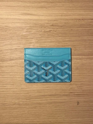 Turkos kortfodral  - Säljer ett stilrent turkost kortfodral från  med det klassiska mönstret i vitt och svart. Fodralet har flera fack för kort och är gjort i läder med canvasdetaljer. Perfekt för dig som vill ha något både snyggt och praktiskt i fickan.