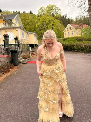 Guldig glittrig långklänning med volanger - Säljer min älskade balklänning med volanger och glitter. Klänningen har flera lager volanger med paljetter och en slits framtill som inte syns om man vill det. Den är i storlek 40 och jag är 174 cm som längdreferens. Skriv för mer bilder eller info, pris kan diskuteras.