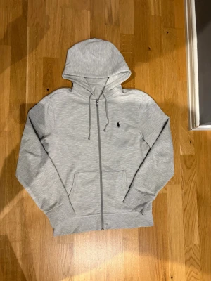 Ljusgrå zip hoodie från Polo Ralph Lauren - Snygg ljusgrå hoodie med dragkedja från Polo Ralph Lauren. Den har tecken på användning. Storlek S.