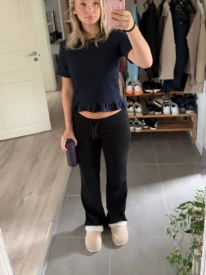 Mörkblå topp med volangkant - Snygg mörkblå topp med korta ärmar och smockad framsida. Toppen har en söt volangkant nedtill och rund halsringning. Perfekt att matcha med både jeans och kjol för en trendig look.