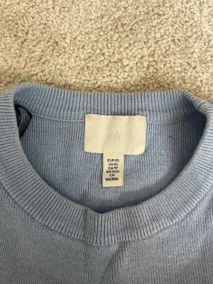 Ljusblå stickad tröja från H&M - En ljusblå stickad tröja från H&M med rund halsringning och korta ärmar. Blev något fel med bilden så tröjan ser lita randig ut på bilden! Väldigt fåtal gånger använd.