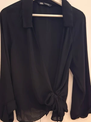 Svart knytblus från Zara - Stilren svart blus från Zara med lång ärm och snygg knytning framtill. Blusen har en klassisk krage och är tillverkad i ett tunt, lätt material som ger ett elegant fall. Tröjan är inte använd (gammal kollektion däremot)🌸
