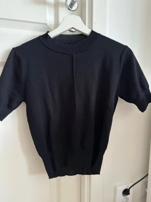 Svart stickad topp - En svart stickad topp med korta ärmar och rund hals. Modellen är enkel och stilren med ribbade kanter vid hals, ärmslut och nederkant. Står inte storlek eller märke. Men skulle säga xs-s. Pris kan diskuteras 