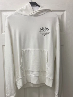Vit hoodie från Amiri - Säljer en clean vit hoodie från Amiri med tryck på bröstet och stor text på ryggen där det står 'Eden Rock St. Barthelemy'. Hoodien har huva och en stor magficka. Tillverkad i mjukt material och har ribbade muddar vid ärmar och nederkant. Perfekt för dig som gillar streetwear.