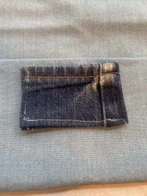 Plånbok i mörkblå denim - Cool plånbok sydd av återvunnet mörkblått denimtyg med kontrasterande orange och vita sömmar. Rektangulär och platt design, perfekt för kort och sedlar. Plånboken har en enkel och stilren look med en touch av vintage.