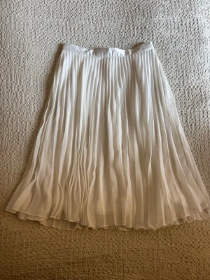 Vit plisserad midikjol - Snygg vit plisserad midikjol med flowig känsla och dragkedja bak. Kjolen har ett elegant fall perfekt för dig som gillar en stilren och fräsch look.