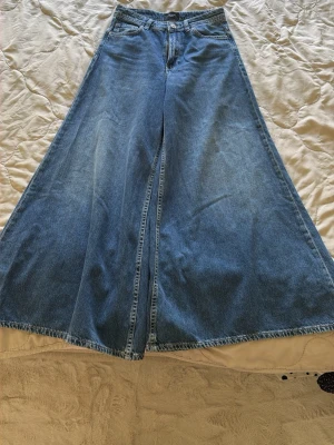 Blåa extremt vida jeans - Säljer ett par blåa jeans med supervid passform och hög midja. Jeansen har klassiska fickor fram och bak, dragkedja och knapp i midjan. Materialet är denim i 100% bomull och benen är riktigt utsvängda för en statement-look.
