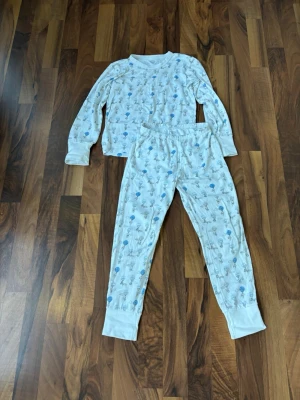 Vit pyjamas med luftballongsmönster Livly - Supersöt vit pyjamas från Livly i 100% bomull med långärmad tröja och byxor. Setet har ett gulligt mönster med små djur som svävar med luftballonger i blått och grått. Perfekt för mysiga kvällar hemma! Barn storlek