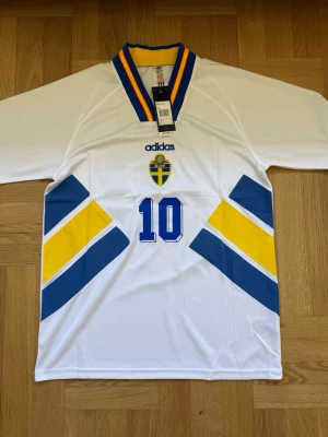Dahlin #10 – Sverige 1994 Borta (storlek M) - Dahlin #10-tryck. Sverige 1994 Borta (vit). Storlek M. Helt ny och aldrig använd. Skickas snabbt 🚚💨  Mått (M): Halvt bröstmått 53 cm • Längd 74 cm • Ärmbredd 23 cm • Axelbredd 44 cm • Ärmlängd 40 cm • Manschett 19 cm.  🔥 Fan Edition – normal passform. 🇸🇪 Sverige landslag.  📩 Skicka gärna ett meddelande vid frågor eller prisförslag! 🛍 Bundle-rabatt upp till 20%! 📦 Skickas samma eller nästa dag.