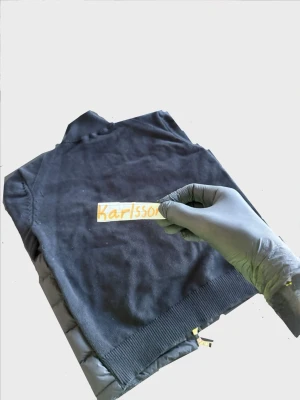 Svart cardigan från Moncler - Kvitto finns me original pris på 8k. Snygg svart cardigan från Moncler med quiltat mönster och stickade svarta ärmar. Cardigan har två framfickor med knappstängning och dragkedja framtill. Klassisk Moncler-logga på bröstet och ribbade muddar vid hals och ärmslut. Perfekt för lager-på-lager-stil.
