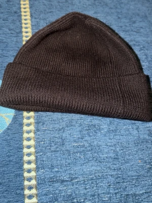 Mörkbrun ribbstickad mössa - Säljer en mörkbrun ribbstickad mössa från A Day's March. Klassisk modell med uppvikt kant och mjukt material som sitter skönt på huvudet. Perfekt för kalla dagar och enkel att matcha med olika outfits.