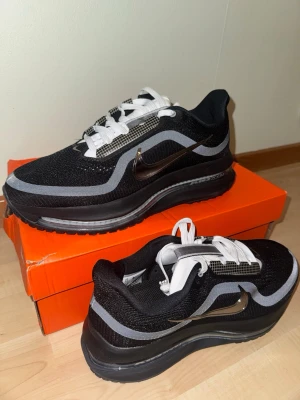Nike Air Max Pegasus Premium svarta och grå sneakers - Nike Air Max Pegasus Premium sneakers i svart mesh med grå och vita detaljer samt en metallic Swoosh på sidan. Skorna har en tjock sula med synlig Air-enhet och vita skosnören. Perfekta för dig som gillar sportig och modern stil.