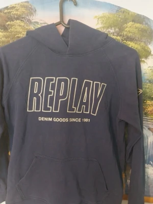 Blå hoodie från Replay - Snygg blå hoodie från Replay med stor vit logga framtill och texten 'Denim Goods Since 1981'. Klassisk känguruficka och huva. Perfekt för en avslappnad streetstyle-look. Tja alla köpare denna tröja är endast tillgänglig efter 4 dagar efter den har lagts ut pga är inte hemma så kan ej skicka men tänkte bara lägga ut en bild så ni ser och ifall när kanske vill köpa efter dessa 4 dgr kan ni få mer bilder från hoddien 