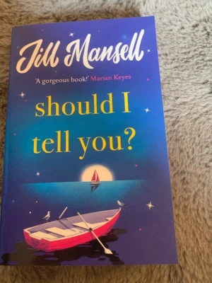 Should I Tell You? av Jill Mansell - En färgstark pocketbok med blå och lila omslag, dekorerad med illustration av en roddbåt och en segelbåt i solnedgång. Romanen handlar om vänskap, kärlek och hemligheter i en brittisk kuststad. Perfekt för dig som gillar romantisk och varm feelgood.