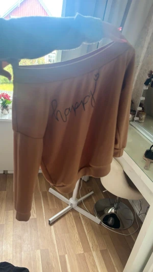 Beige sweatshirt med texten happy - Säljer en beige sweatshirt med lång ärm och texten 'happy' skrivet i svart med ett litet hjärta på bröstet. Tröjan har rund halsringning och ribbade muddar vid ärmslut och nederkant. Perfekt för en chill och avslappnad stil.