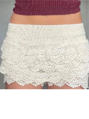 Vita virkade shorts med volang - Supersöta vita virkade shorts med flera lager volangdetaljer. De har hög midja och ett elastiskt band upptill för skön passform. Perfekta till sommaren och ger en romantisk och bohemisk vibe.