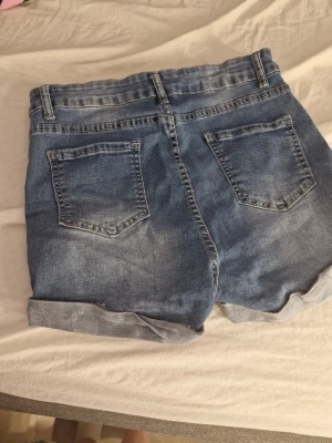 Blå denimshorts från SHEIN - Snygga blå denimshorts från SHEIN med klassisk femficksdesign och uppvikta benslut. Shortsen har hög midja och stängs med dragkedja och knapp. Perfekta för varma dagar och enkla att matcha med olika toppar.