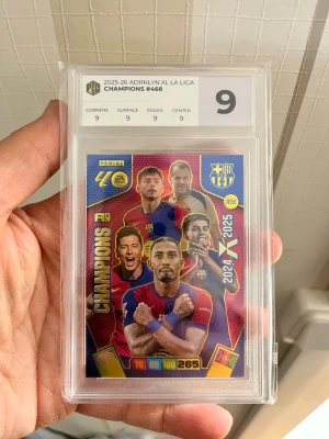 Panini Adrenalyn XL Champions #468 - Säljer ett samlarkort från Panini Adrenalyn XL 2025-26 La Liga, Champions #468. Kortet är graderat 9 av PCG och visar flera spelare från FC Barcelona i färgstark design. Kortet är inplastat i skyddsfodral och har detaljerade stats på framsidan.