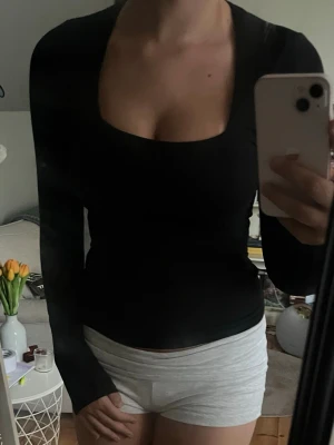 Svart långärmad topp med fyrkantig ringning - Säljer en svart långärmad topp med snygg fyrkantig ringning. Modellen är tight och enkel, perfekt att styla med olika outfits. Materialet ser ut att vara stretchigt och mjukt, vilket gör den bekväm att bära.