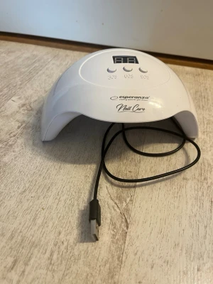 UV LED nagellampa Esperanza - UV LED nagellampa från Esperanza med digital display och tre timerinställningar (30s, 60s, 90s). Lampan är vit, har en halvmåneformad design och ansluts via USB-kabel. Perfekt för att härda gelélack och andra nagelprodukter hemma.