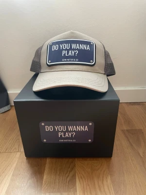 John hatten keps  - John hatten keps med motivet DO YOU WANNA PLAY? Brickan är i metall skick 8/10 storlek one size 😊👍🏼 vid mer bilder eller frågor bara att skriva ✅😌