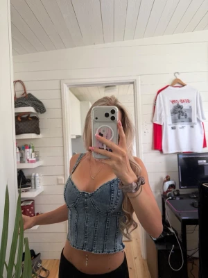 Blå denim korsettopp med sömmar - Säljer en snygg blå korsettopp i denim med markerade sömmar och smala axelband. Toppen är croppad och har en figurnära passform som framhäver midjan. Perfekt att styla med höga jeans eller kjol för en trendig look.