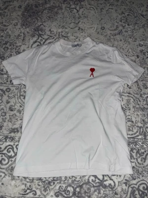 Vit t-shirt med rött hjärta och A - Säljer en vit T-shirt med ett rött hjärta med ett stort A under, den är väldigt skön att ha på sig och perfekt nu till sommaren. Den är inte varm att ha på sig, utan det är väldigt skönt material.