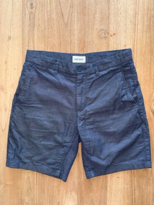 Blåa shorts från East West - Snygga blåa shorts från East West med klassisk passform. De har sidofickor, bälteshällor och knäppning fram. Baktill finns två fickor med knapp. Perfekta för varma dagar och enkel att matcha med olika stilar. Storlek 29”