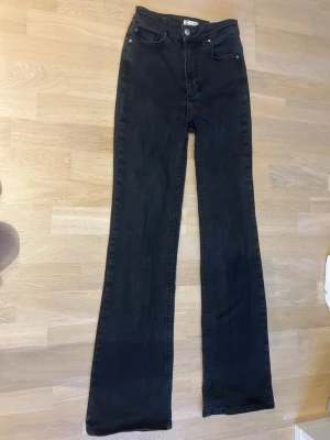 Svarta bootcut jeans med hög midja - Säljer ett par svarta bootcut jeans med hög midja och klassisk femficksmodell. Jeansen har vida ben och stängs med knapp och dragkedja. Perfekta för dig som gillar en retroinspirerad look och vill ha ett par bekväma jeans i garderoben.