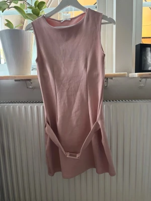 Rosa ärmlös klänning från ZARA - Söt ljusrosa ärmlös klänning från ZARA med rund halsringning och tillhörande bälte i midjan. Klänningen har en enkel, rak passform och är tillverkad i ett mjukt tyg som känns bekvämt mot huden. Perfekt för en stilren och trendig look.