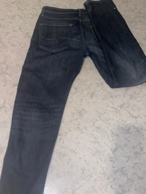 Mörkblå raka jeans - Säljer ett par mörkblå jeans med raka ben och klassisk femficksdesign. Jeansen har kontrastsömmar och en snygg tvättad look med lätt slitningar framtill. Perfekta till en avslappnad stil och passar till det mesta i garderoben.