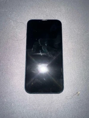 Svart iPhone med dubbla kameror - Säljer en marin blå iPhone 13 med stilren design och rundade hörn. Baksidan har två kameror placerade i hörnet och den klassiska Apple-loggan i mitten. Mobilen har en glasbaksida och metallram. Perfekt för dig som gillar snygg och modern teknik.