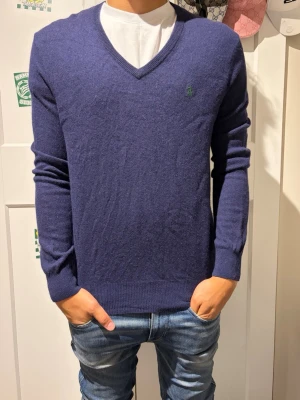 Mörkblå V-ringad tröja Ralph lauren  - Mörkblå V-ringad tröja i mjukt stickat material. Tröjan har långa ärmar, ribbade muddar och en diskret broderad logga på bröstet. Perfekt att bära över en t-shirt eller skjorta för en stilren look.