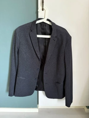 Mörkgrå kavaj från Selected Homme - Stilren mörkgrå kavaj från Selected Homme med två knappar framtill och klassisk krage. Kavajen har två fickor och är helfodrad med svart innerfoder. Perfekt för en dressad look och passar till många olika outfits. Står tyvärr ingen storlek men sitter som en Medium. 
