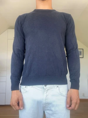 Mörkblå stickad tröja - Mörkblå stickad tröja ifrån Hansen & Jacob tillverkad i 100% bomull. Strl S. Den högra armbågspatchen har en väldigt liten skada (se bild 5). Modellen är 178 cm och väger 77 kg. Hör gärna av dig vid frågor!
