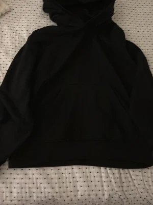 Svart hoodie med magficka - En klassisk svart hoodie med huva och stor magficka framtill. Hoodien har en enkel och clean design utan tryck eller mönster, perfekt för en avslappnad stil. Tillverkad i mjukt material som känns skönt mot huden. Passar dig som gillar basic och stilrent.