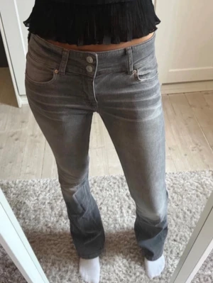 Lowwaist Jeans  - Säljer ett par gråa bootcut jeans med hög midja och tre knappar i gylfen. Jeansen har en lätt tvättad look och sitter tight över låren för att sedan bli vidare nedtill. Perfekta till en trendig vardagsstil.