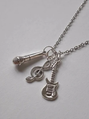 Halsband med musikinspirerade berlocker - Snyggt silverfärgat halsband med tre berlocker: en mikrofon, en gitarr och en g-klav. Kedjan är tunn och smidig, och berlockerna har detaljerade former som passar perfekt. Materialet rostfritt stål.