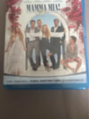 Mamma Mia! Blu-ray fodral - Säljer ett Blu-ray fodral till filmen Mamma Mia! med färgstarkt omslag där flera karaktärer syns mot en vit bakgrund med rosa blommor. Perfekt för dig som gillar musikaler och vill ha något extra till filmsamlingen.