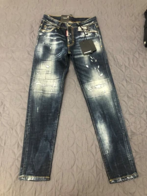 Dsquared 2  - Säljer ett par mörkblå dsquared 2 jeans med slitningar och tvättade effekter på både fram- och baksida. Jeansen har raka ben, klassisk femficksmodell och kontrastsömmar. Materialet är denim och de har en modern, trendig look. Storleken är 38 på byxorna men 30 i verkligheten. Helt ny utan prislapp.