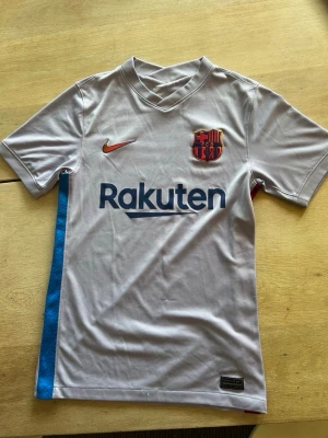 Grå FC Barcelona matchtröja Nike - Det står arr tröjan är xs fast den är stor i storleken så den är S. Snygg grå FC Barcelona matchtröja från Nike med klubbmärke och Rakuten-logga på bröstet. Tröjan har blå och röda detaljer på sidorna, korta ärmar och är tillverkad i ett lätt, ventilerande material som passar perfekt till fotbollsträning.