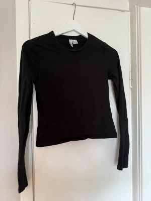 Svart långärmad topp från H&M Divided - En enkel och stilren svart långärmad topp från H&M Divided. Modellen är figurnära med rund halsringning och tillverkad i mjuk bomull. Perfekt basplagg att matcha med olika outfits.