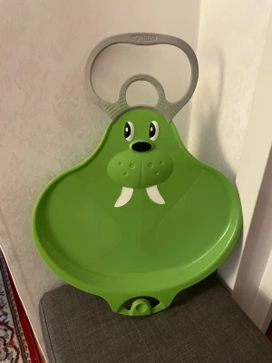 Grön pulka med handtag för barn - Grön pulka med roligt djurmotiv och stort grått handtag upptill. Har en rund sittdel och fotstöd längst fram som gör den lätt att hålla i backen. Knappt använd.