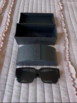 Svarta solglasögon från Prada - Snygga svarta solglasögon från Prada med breda, rektangulära bågar i blank plast. Kommer med originalfodral och låda. Perfekta för dig som vill ha en stilren och trendig accessoar till sommaren.    Helt perfekt till sommaren och att åka utomlands ! 🩵🩵